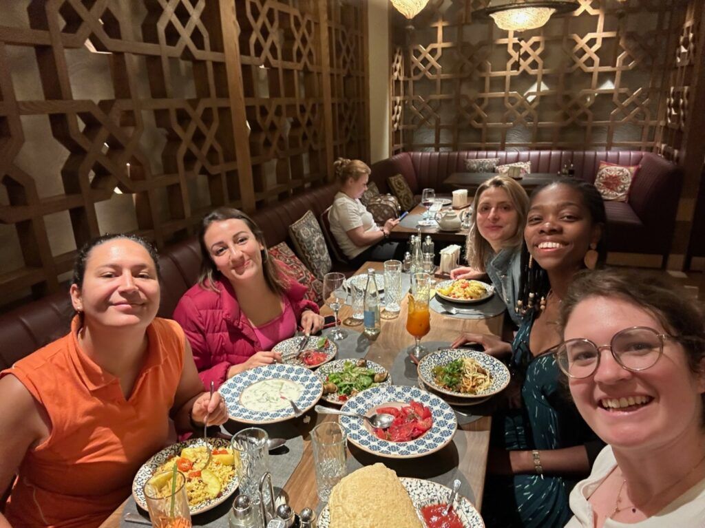 Eine Gruppe von WeRoad-Reisenden lächelt beim gemeinsamen Abendessen in einem traditionell dekorierten Restaurant in Usbekistan.