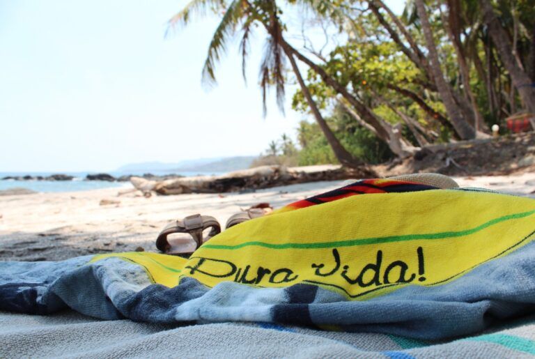 Gelbes Handtuch mit der Aufschrift „Pura Vida!“ an einem Sandstrand in Costa Rica.