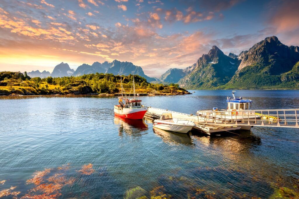 Ein rotes Fischerboot liegt an einem Steg im Trollfjord auf den Lofoten, umgeben von majestätischen Bergen unter einem farbenfrohen Abendhimmel.