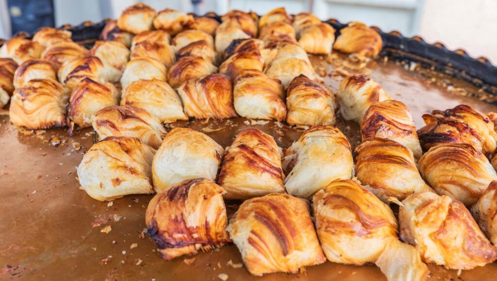 Frisch gebackene, goldbraune Somsa-Teigtaschen auf einem großen Backblech in Usbekistan.