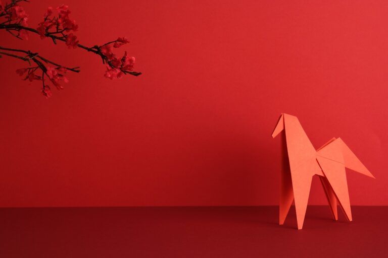 Ein rotes Origami-Pferd mit Kirschblüten auf rotem Hintergrund zum chinesischen Neujahr 2026.