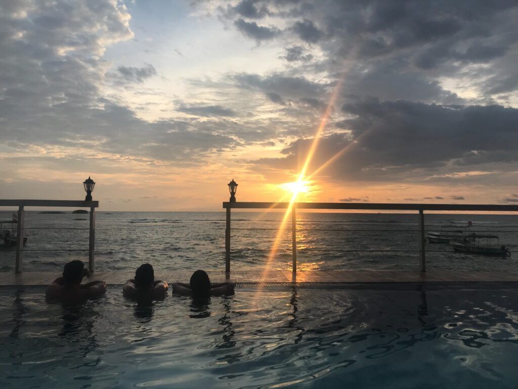 Drei Personen genießen den Sonnenuntergang über dem Meer von einem Infinity-Pool in Sri Lanka aus.