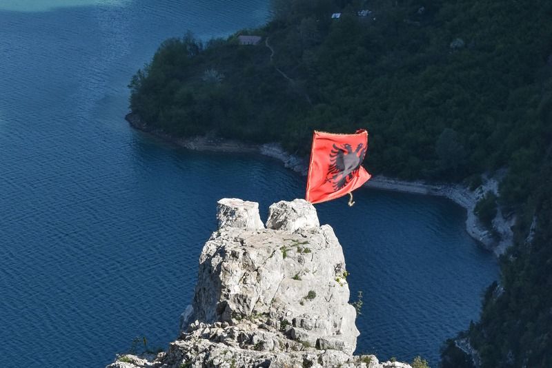 Albanische Nationalflagge auf einem weißen Felsgipfel hoch über dem tiefblauen Komani-See in den albanischen Alpen