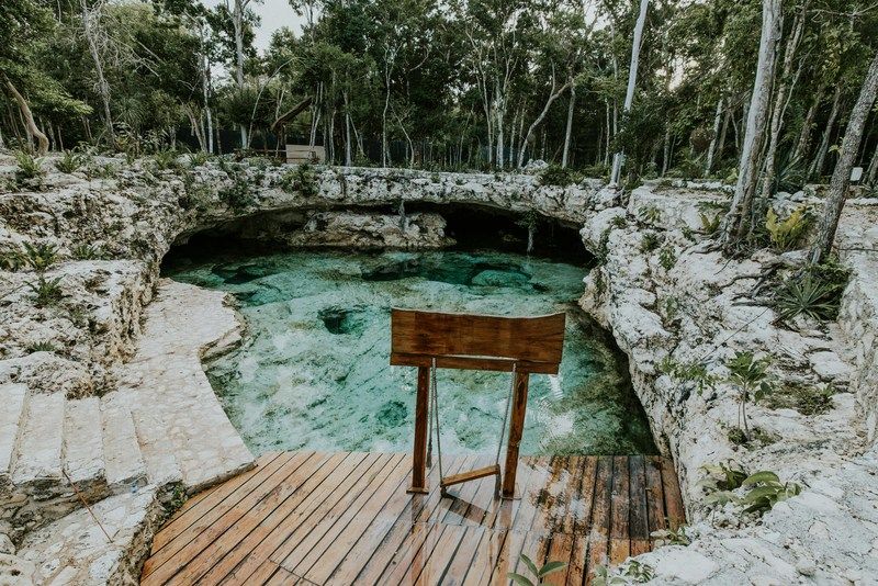 Offener Cenote mit Holzsteg und Hinweisschild im Dschungel von Yucatán, Mexiko