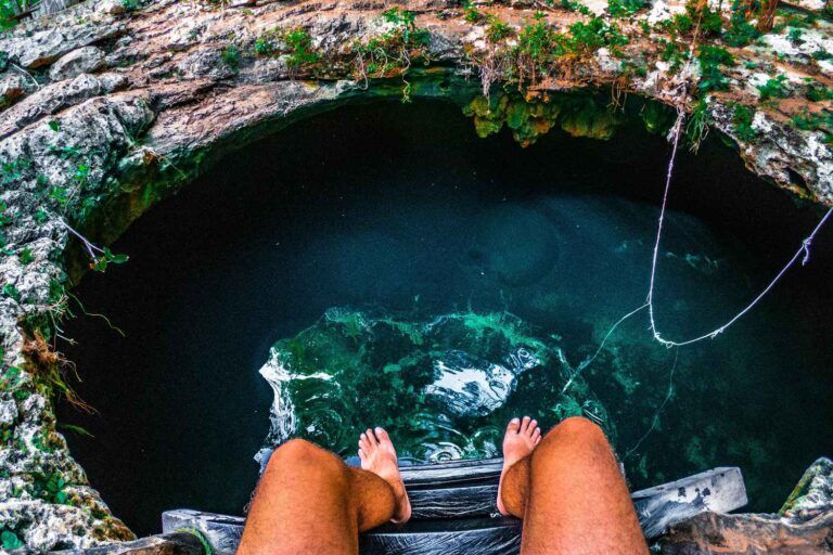 Beine über dem türkisfarbenen Wasser eines Cenote in Yucatán, Mexiko – Sprung ins kühle Nass aus der Ich-Perspektive