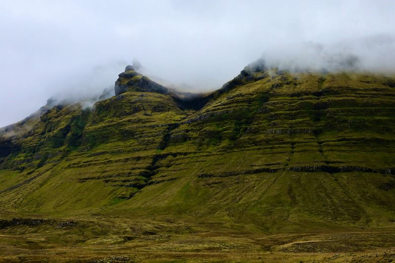 Grüne Basaltberge mit tiefen Wolken über einer wilden nordischen Landschaft in Island
