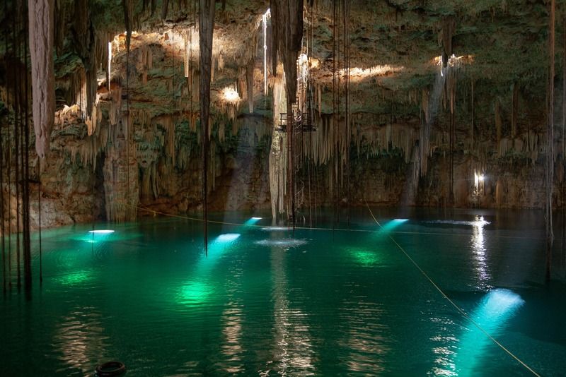 Unterirdischer Höhlen-Cenote mit Stalaktiten und Lichtstrahlen über türkisem Wasser, Yucatán, Mexiko