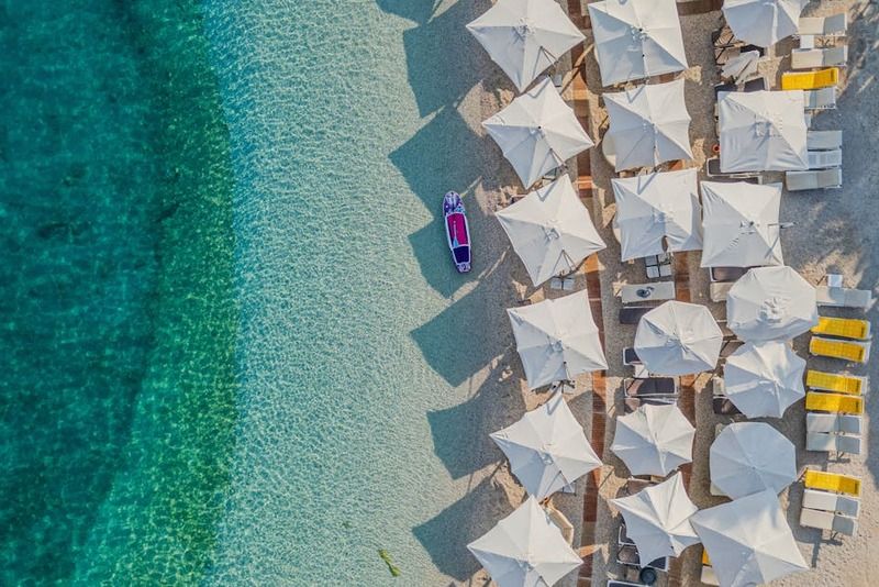 Luftaufnahme eines albanischen Strandes mit weißen Sonnenschirmen, Liegestühlen und türkisfarbenem Meer