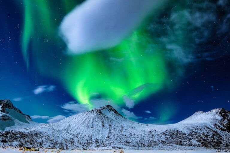 Spektakuläres grünes Nordlicht wirbelt dramatisch über schneebedeckte Berggipfel in Norwegen bei klarem Winterhimmel