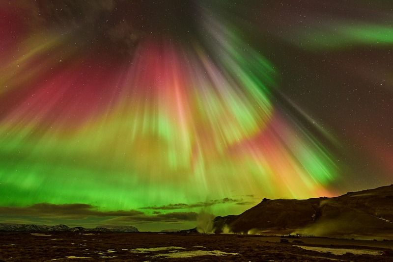 Nordlichter in Rot, Gruen und Gelb ueber einer verschneiten Berglandschaft in der Nacht