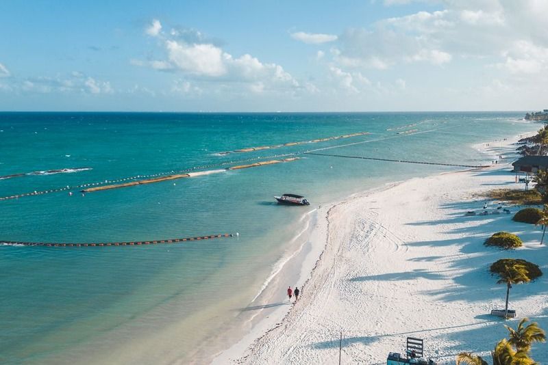 Luftaufnahme eines weißen Karibikstrands mit türkisfarbenem Meer, zwei Spaziergängern und Palmenresort an der Riviera Maya, Mexiko