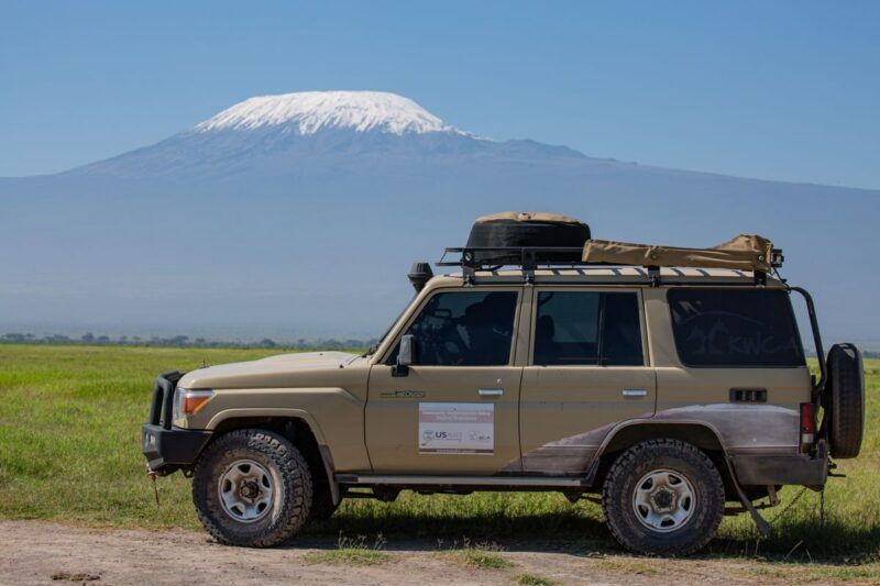 Ein Geländewagen, der vor dem Kilimandscharo geparkt ist, mit Abenteuertouren und malerischen Landschaften im Hintergrund.