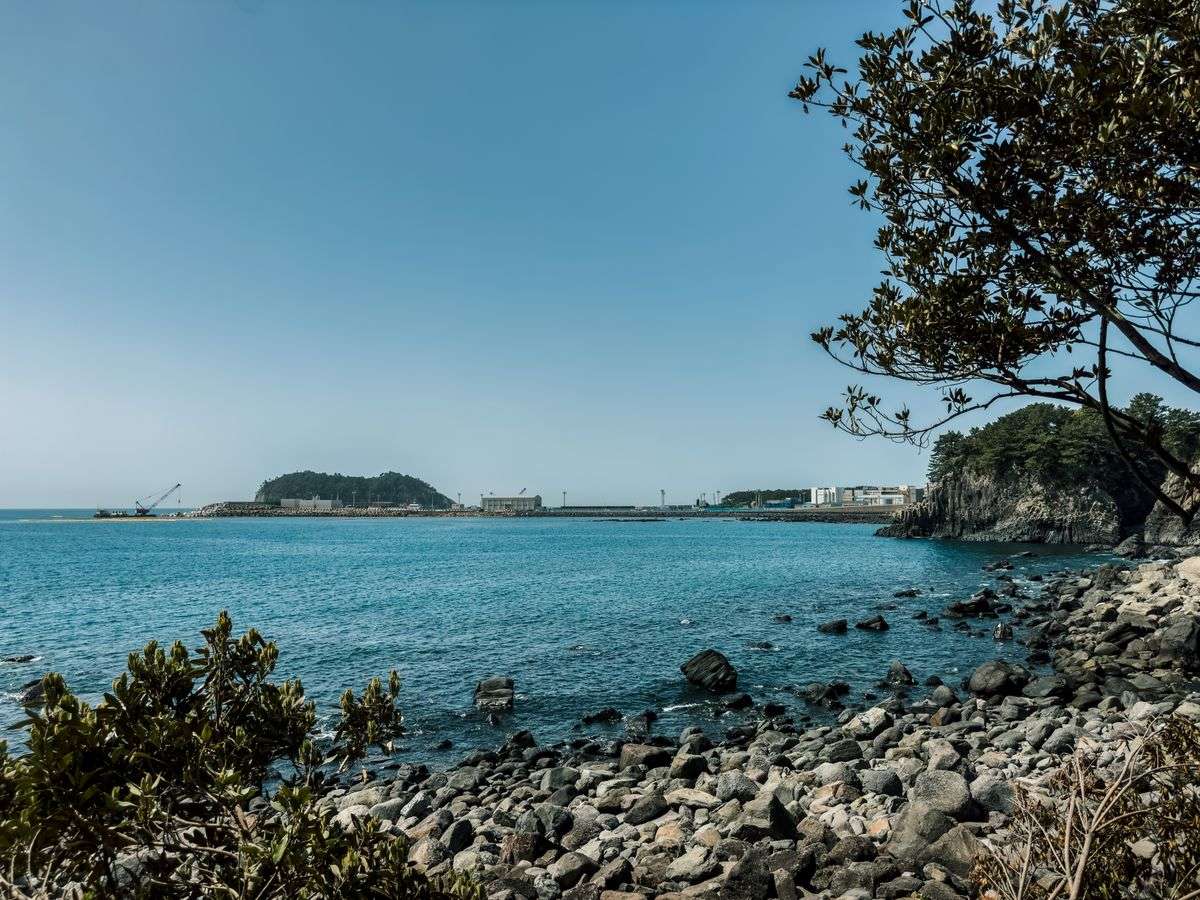 Felsige Küste mit ruhigem Meer, blauem Himmel und niedrigen Inseln im Hintergrund