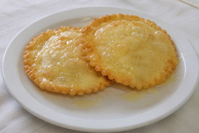 Zwei knusprig frittierte Teigtaschen, glänzend mit goldenem Honig übergossen, auf einem weißen Teller