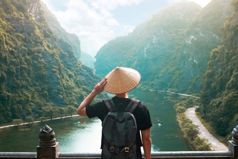 Reisender von hinten mit vietnamesischem Kegelhut blickt auf das Karsttal von Trang An in Vietnam