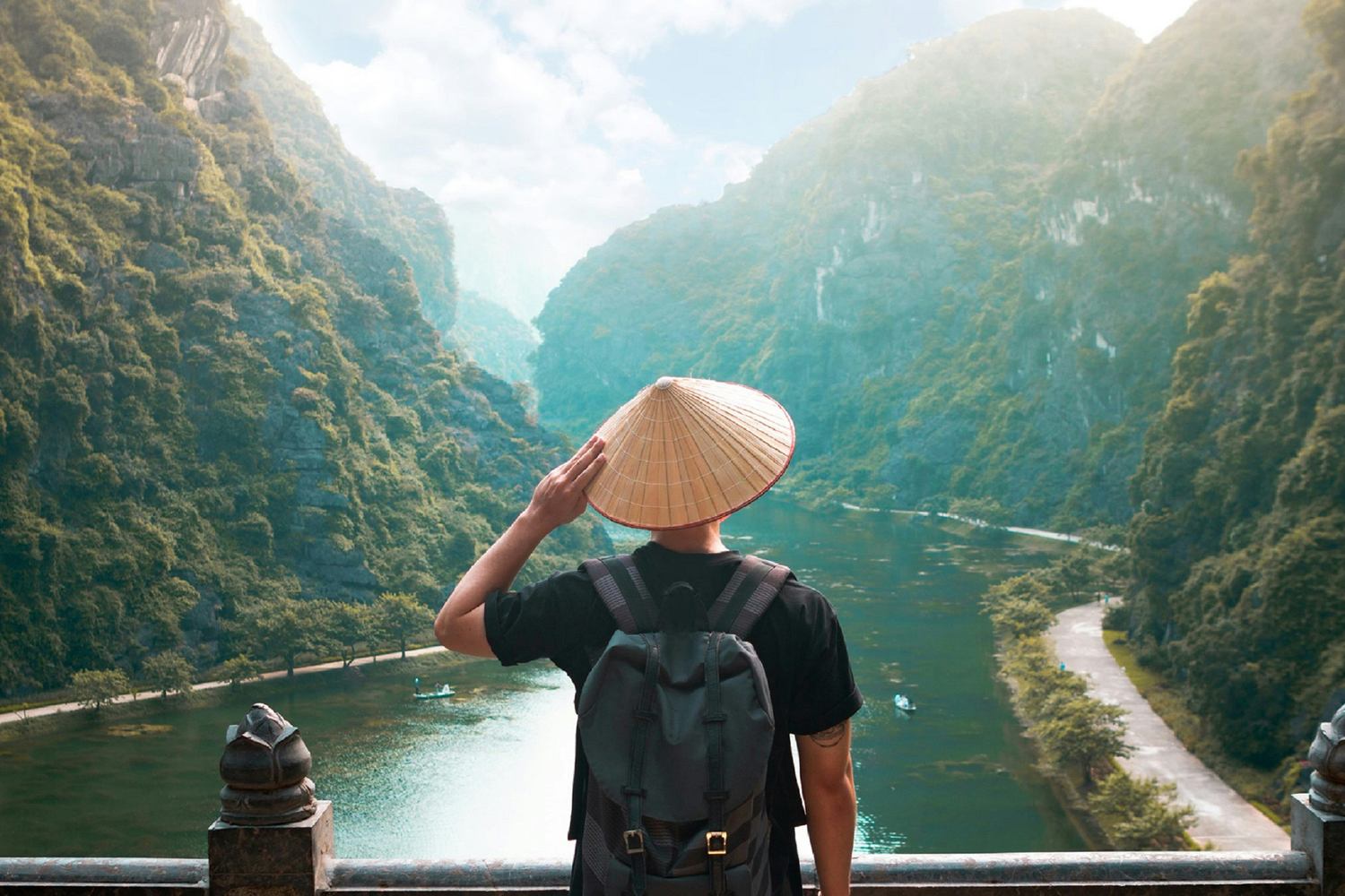 Reisender von hinten mit vietnamesischem Kegelhut blickt auf das Karsttal von Trang An in Vietnam