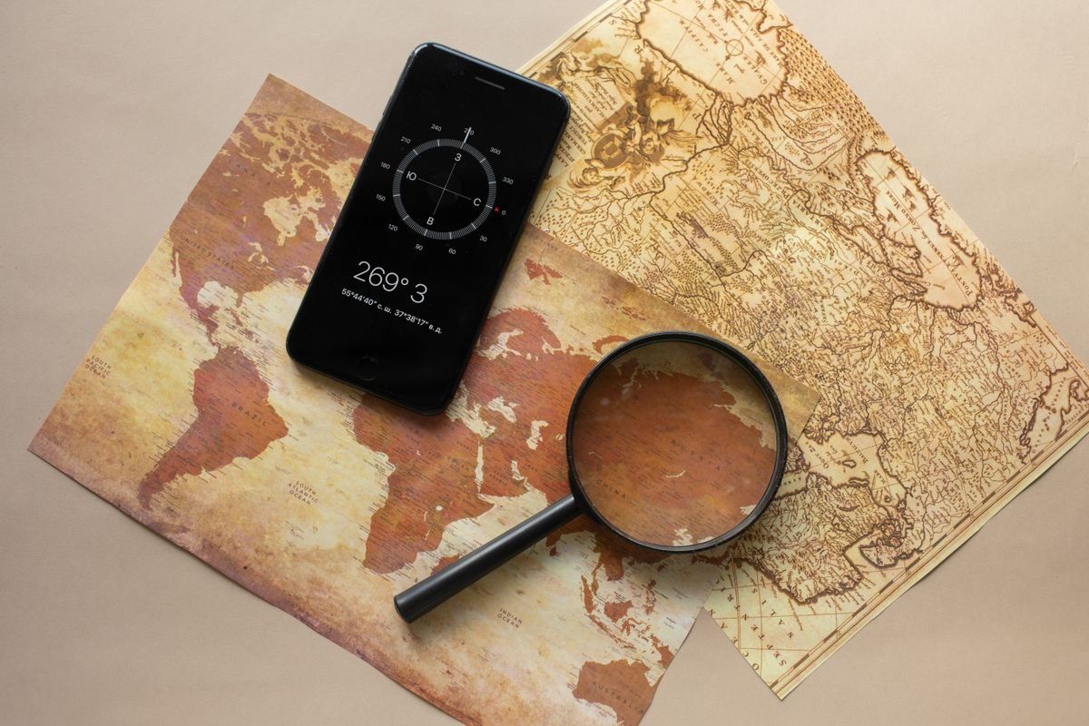 Smartphone mit Kompass-App und Lupe auf zwei alten Landkarten