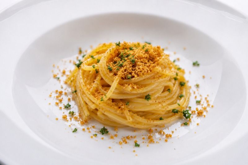 Spaghetti mit knusprigen Semmelbröseln und frischer Petersilie, elegant auf einem weißen Teller angerichtet