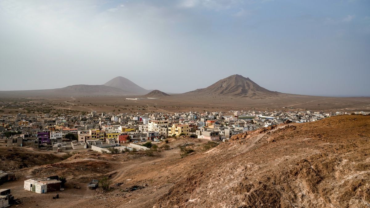 Stadt in trockener Vulkanlandschaft mit kargen Hügeln und zwei Bergen unter hellem Himmel