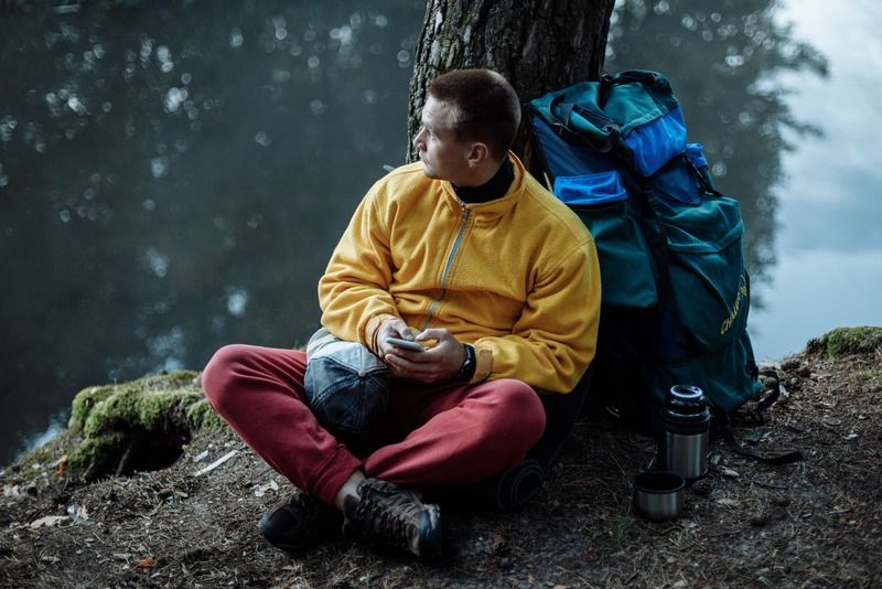 Wanderer macht Pause an einem See mit Rucksack und Thermoskanne während einer Wanderung