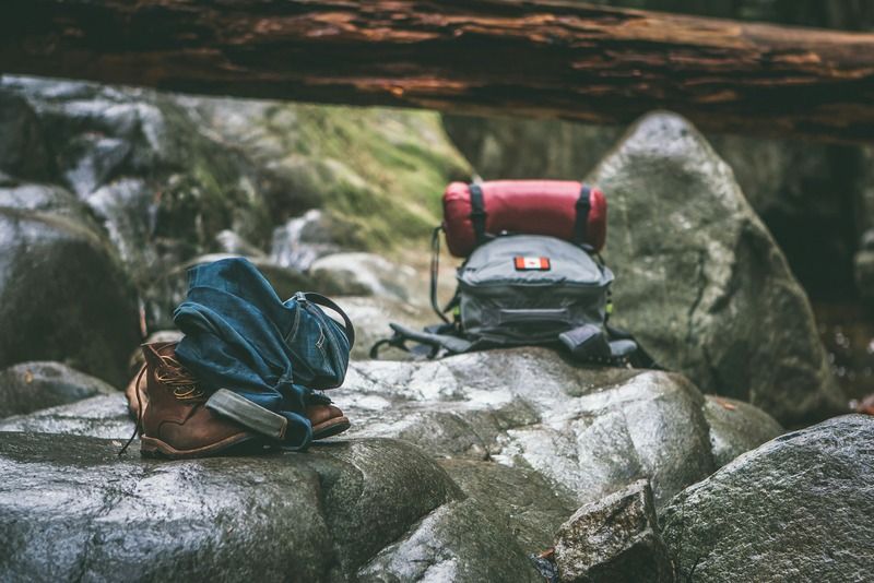 Wanderschuhe, hochgekrempelte Jeans und ein Camping-Rucksack liegen auf Felsen im Wald
