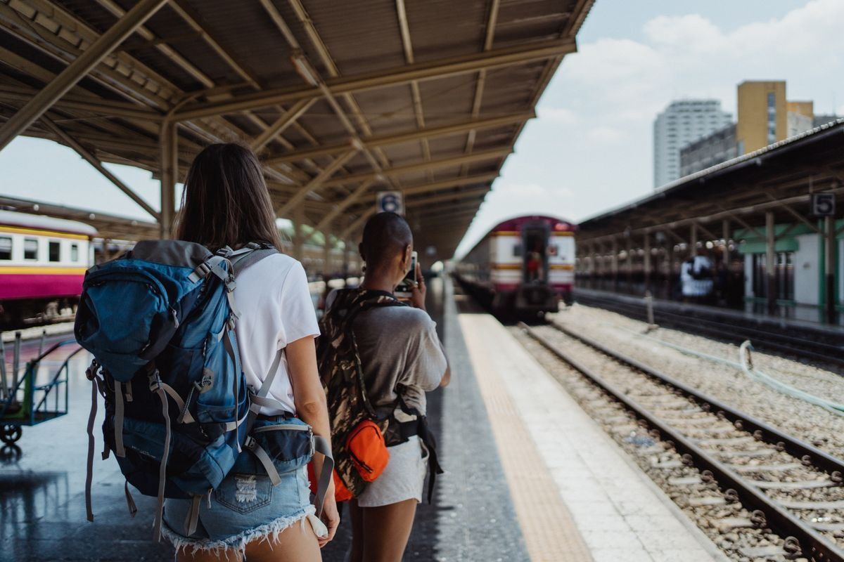 Zwei Backpacker mit Rucksäcken warten auf einem Bahnsteig neben den Gleisen