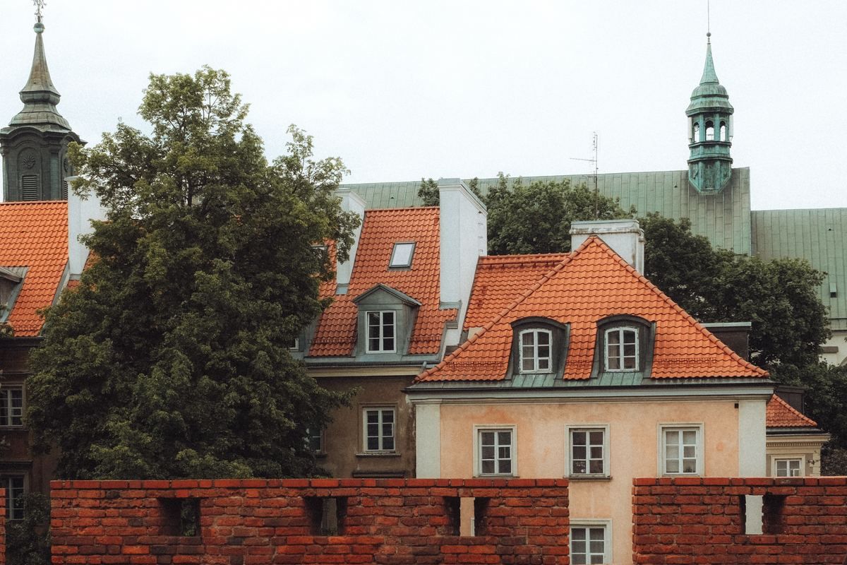 Altstadthäuser mit roten Ziegeldächern, Bäumen und Kirchturm in Warschau