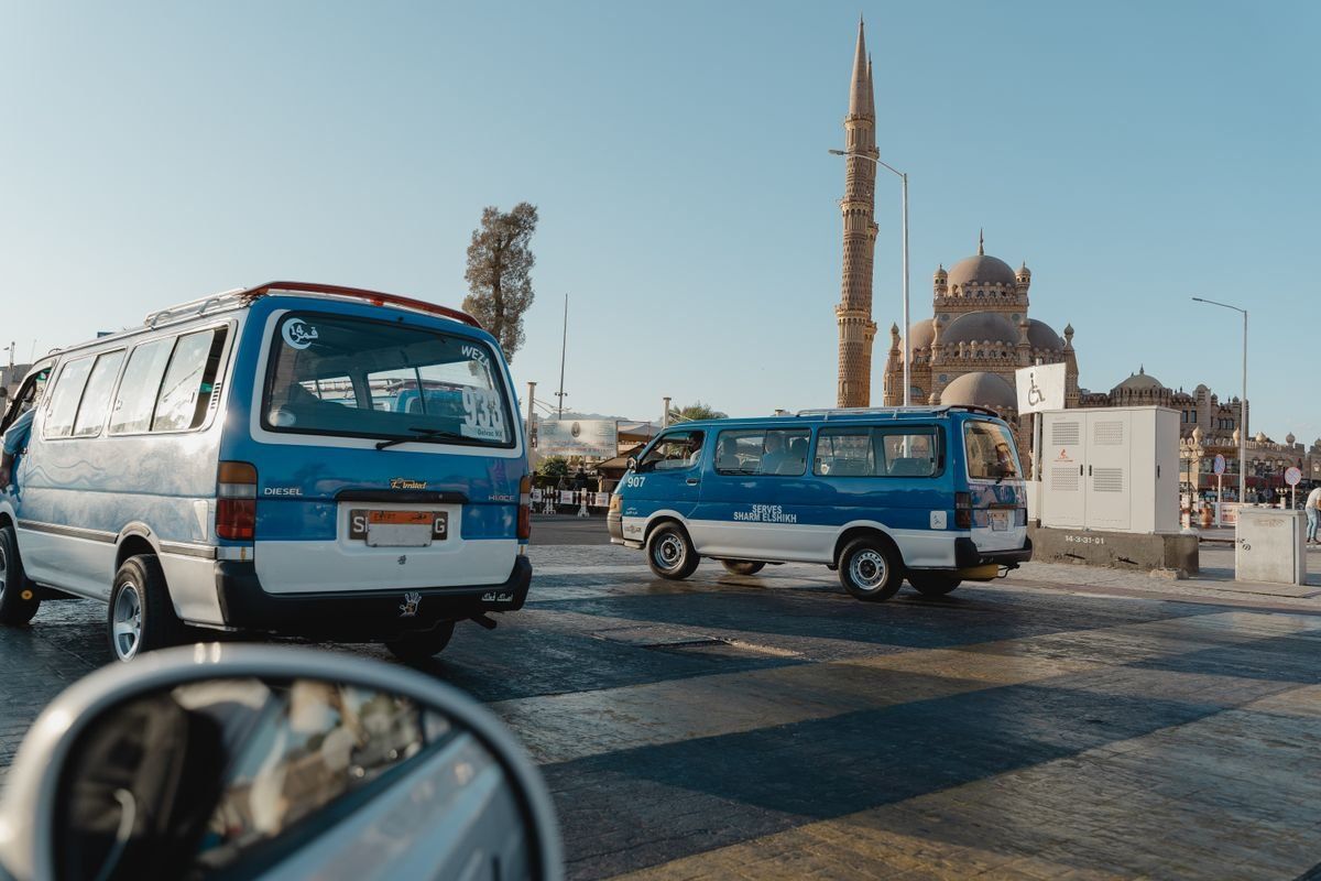 Blaue Kleinbusse auf einer Straße vor einer Moschee mit Minarett