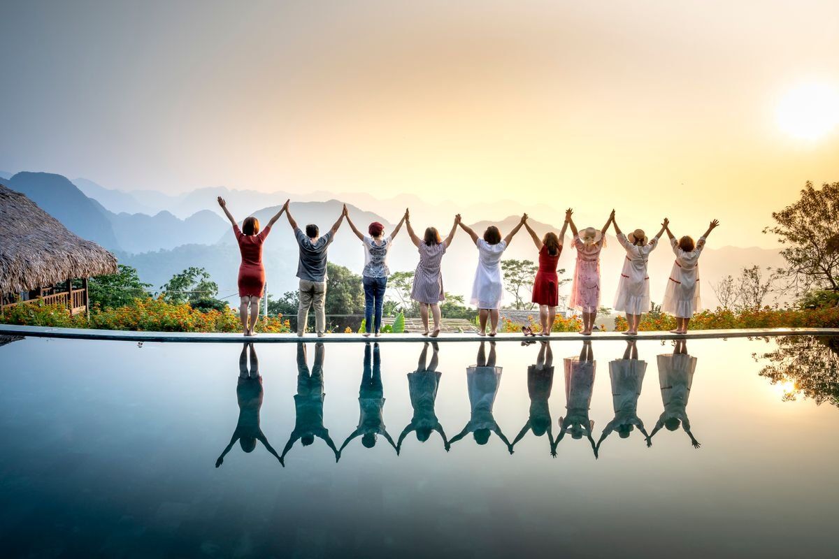 Gruppe von Menschen steht Hand in Hand vor Sonnenuntergang an einem spiegelnden Pool mit Bergblick