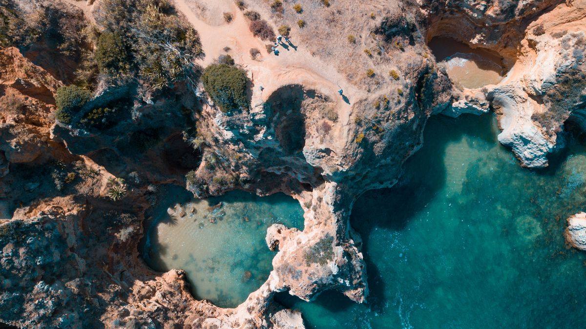 Luftaufnahme von zerklüfteten Felsen und türkisfarbenen Wasserbecken an der Küste