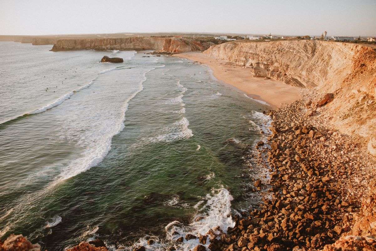 Rauhe Steilküste mit felsigem Ufer, Strand und anrollenden Wellen im warmen Abendlicht