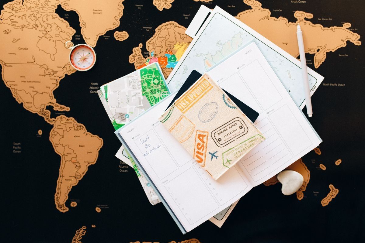 Reiseunterlagen mit Pass, Notizbuch, Stadtplan und Kompass auf einer Weltkarte