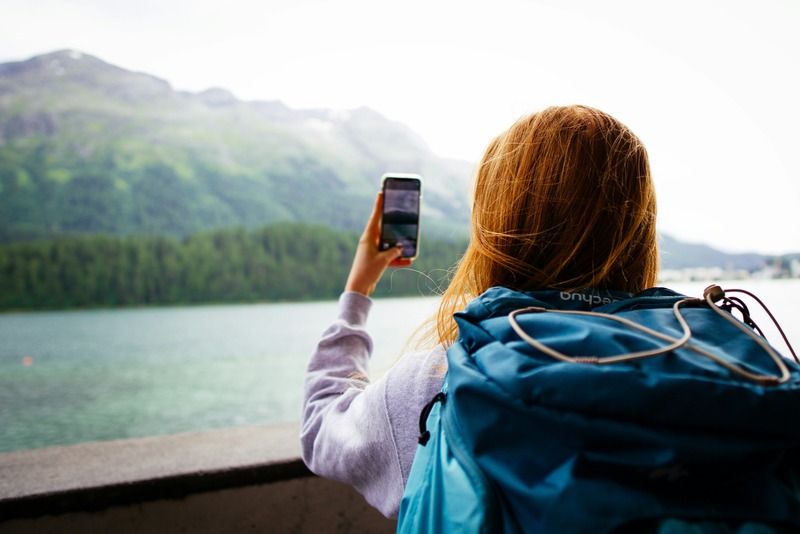 Rucksacktouristin fotografiert mit dem Handy einen türkisfarbenen Alpensee umgeben von grünen Bergen