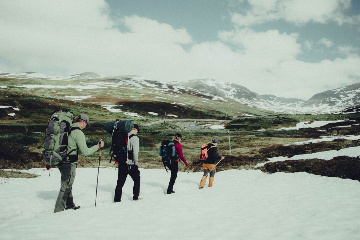 Vier Wandernde mit Rucksäcken überqueren ein Schneefeld in offener Berglandschaft
