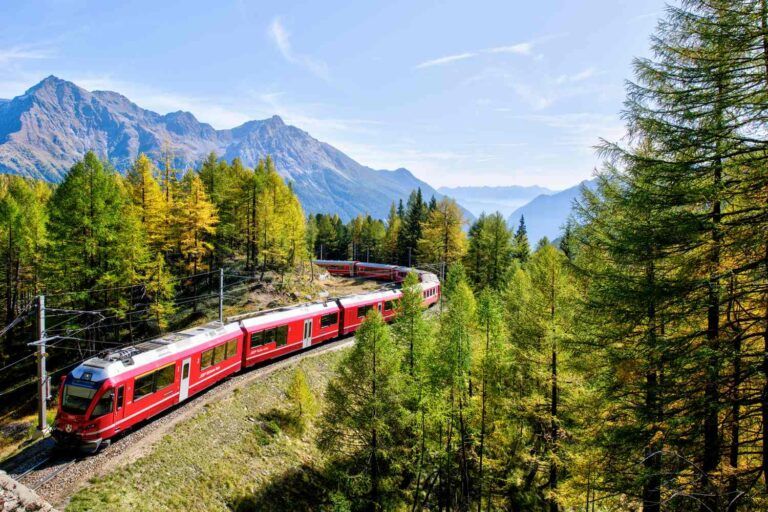 Roter Schmalspurzug fährt durch einen goldenen Lärchenwald im Herbst in den Schweizer Alpen