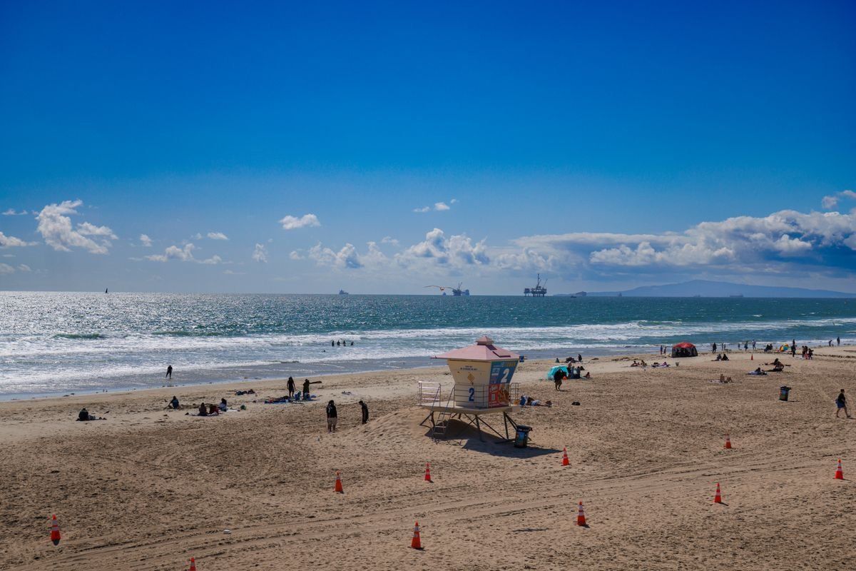 Breiter Sandstrand mit Rettungsturm, verstreuten Badegästen und Schiffen am Horizont
