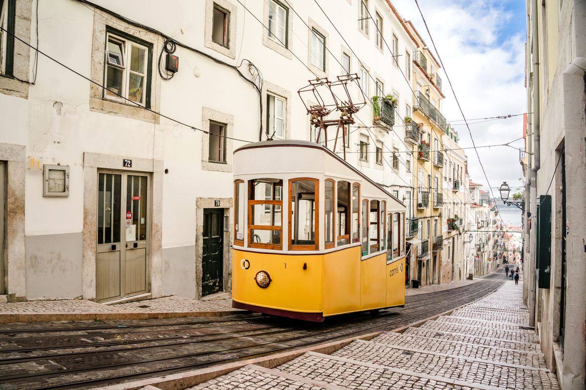 Gelbe Straßenbahn fährt durch eine enge Straße mit hellen Häusern in Lissabon
