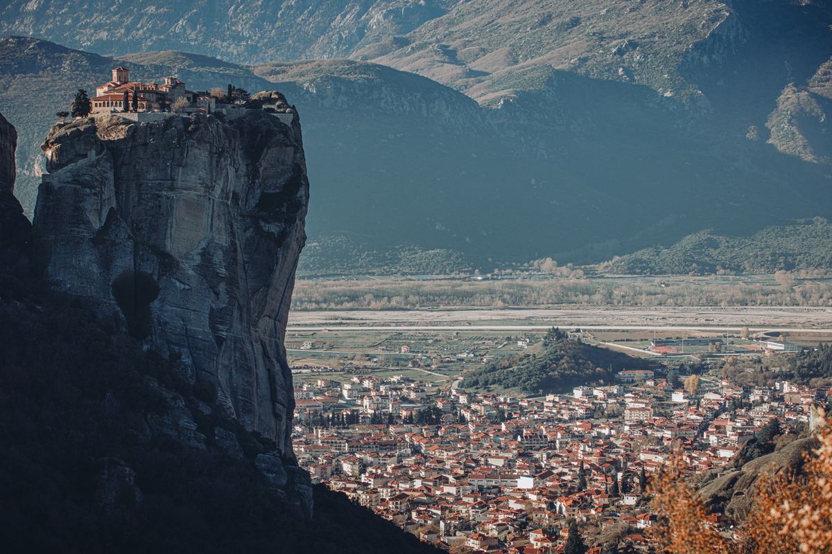 Kloster auf hohem Felsen über einer Stadt im Tal vor bergiger Kulisse