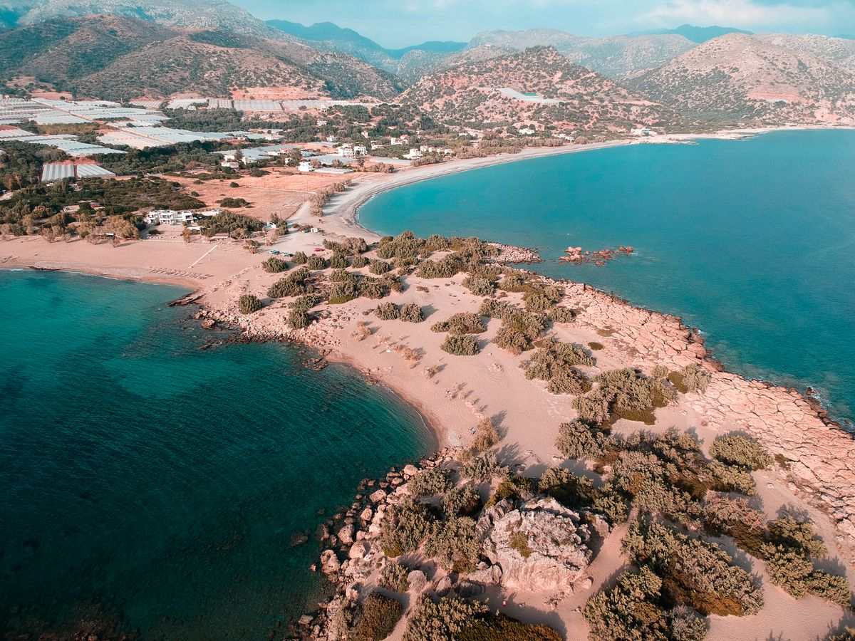 Luftaufnahme einer sandigen Landzunge mit türkisfarbenem Wasser und Bergen im Hintergrund