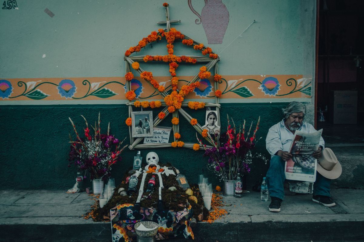 Straßenaltar mit orangefarbenen Blumen, Fotos und Kerzen neben einem sitzenden Mann