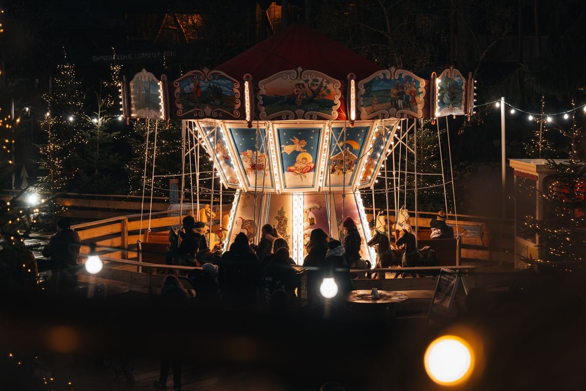 Beleuchtetes Kettenkarussell auf einem Weihnachtsmarkt bei Nacht mit Menschen im Vordergrund