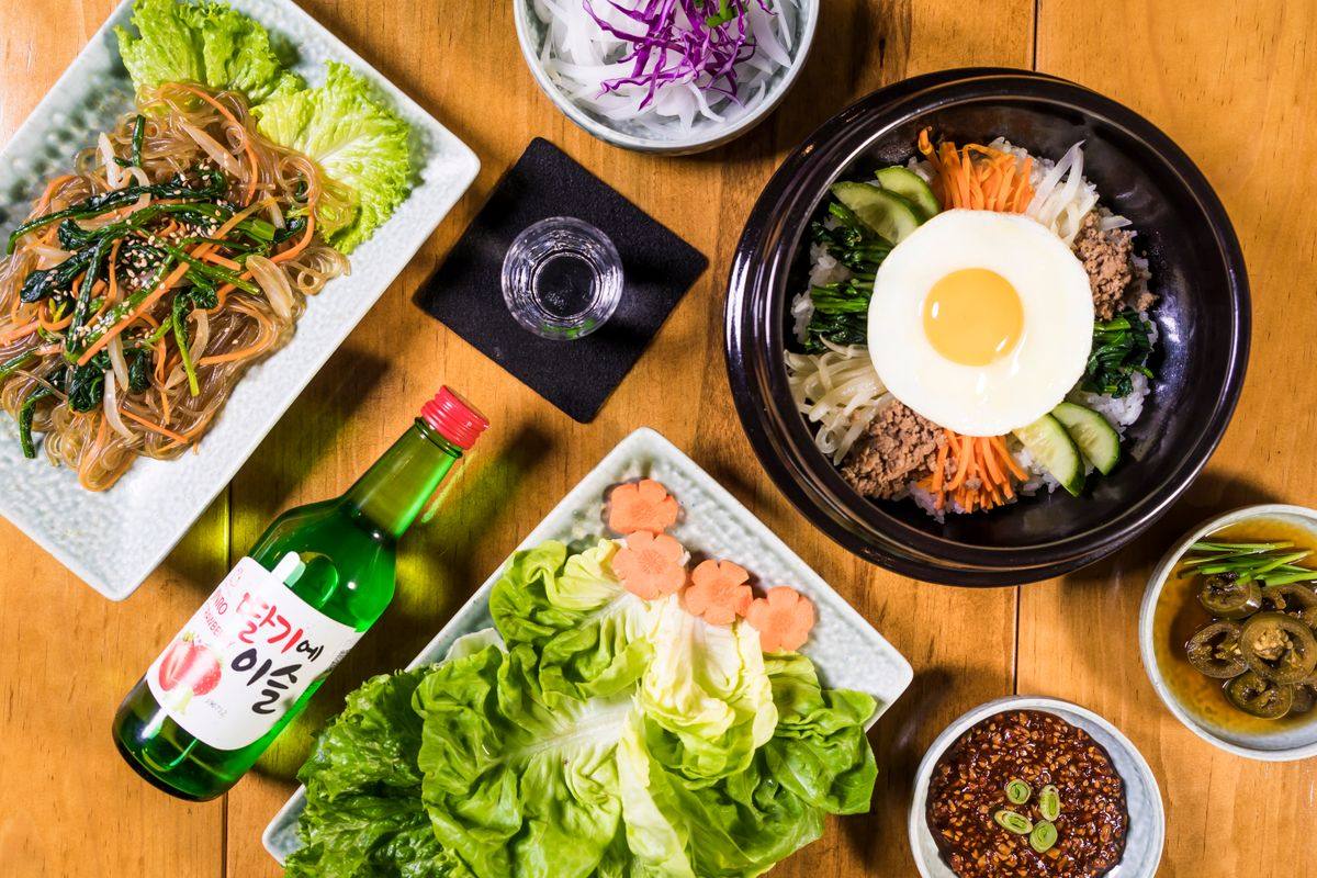 Bibimbap, Japchae, Soju und Beilagen auf einem Holztisch von oben
