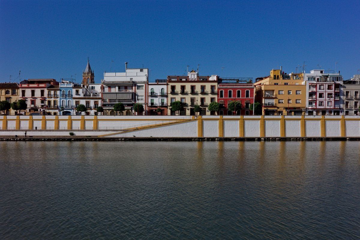 Bunte Häuserzeile am Ufer des Guadalquivir unter klarem blauem Himmel