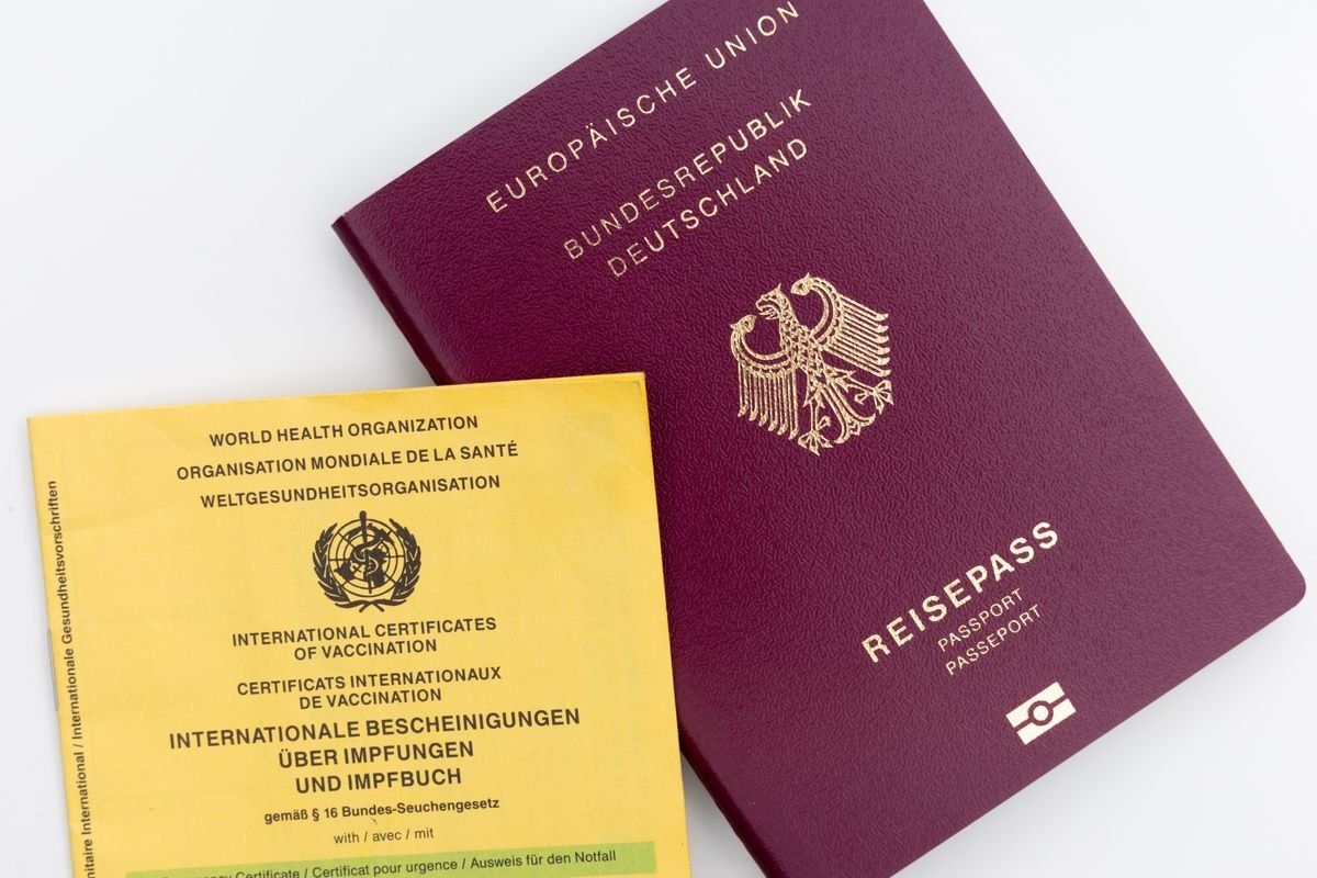 Deutscher Reisepass neben gelbem internationalen Impfpass auf weißem Untergrund