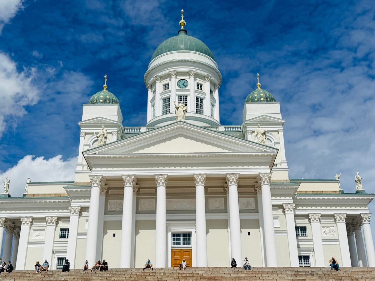 Frontansicht des Helsinki-Doms unter blauem Himmel mit Menschen auf den Stufen