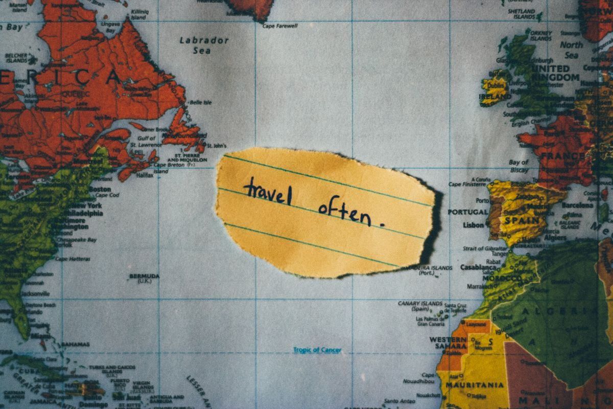 Gelber Zettel mit der Aufschrift travel often auf einer Weltkarte zwischen Nordamerika und Europa