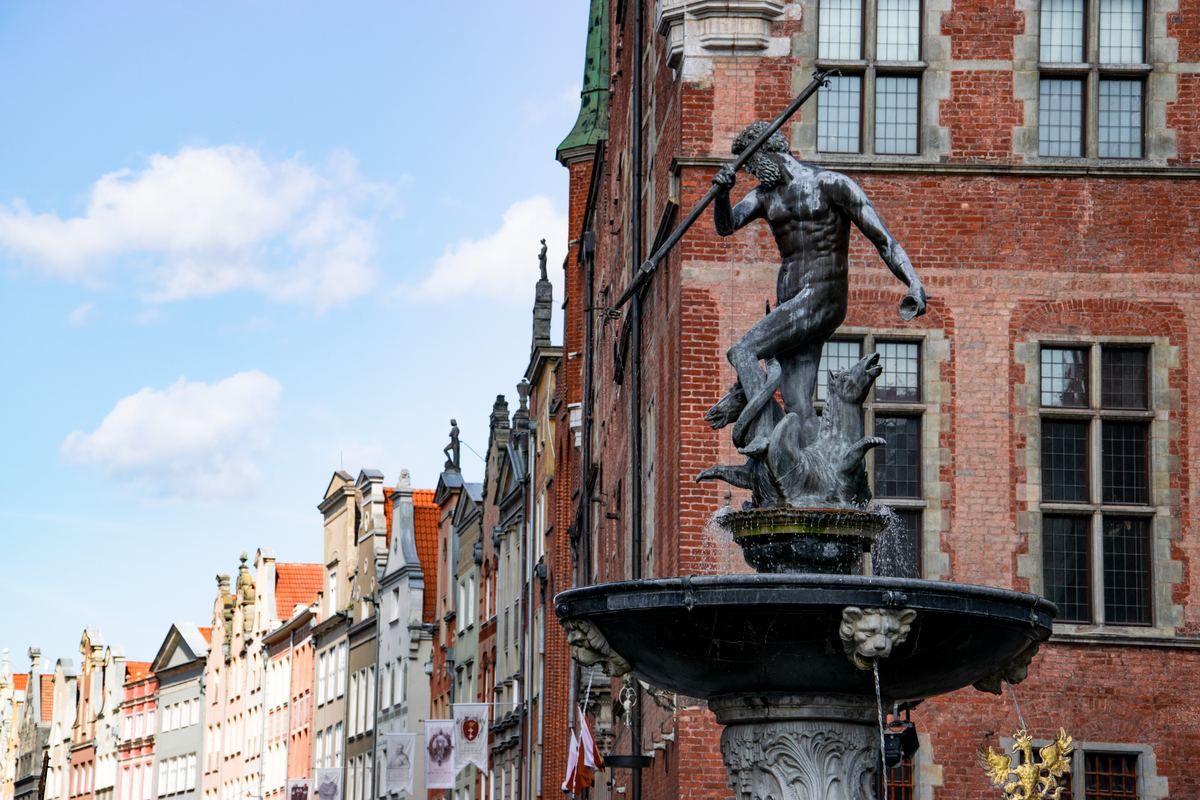 Neptunbrunnen vor historischer Backsteinfassade und schmalen Altstadthäusern in Danzig