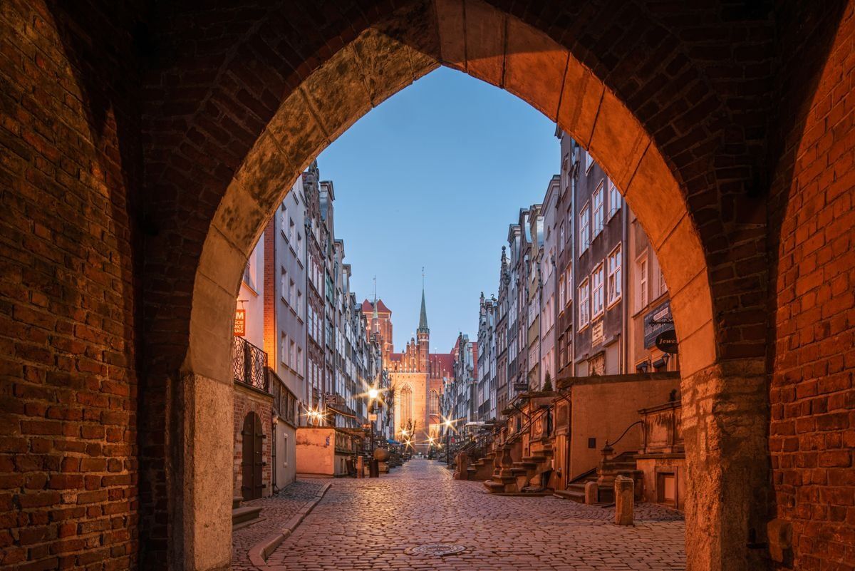 Pflastergasse in der Danziger Altstadt bei Abendlicht, gesehen durch einen Backsteinbogen