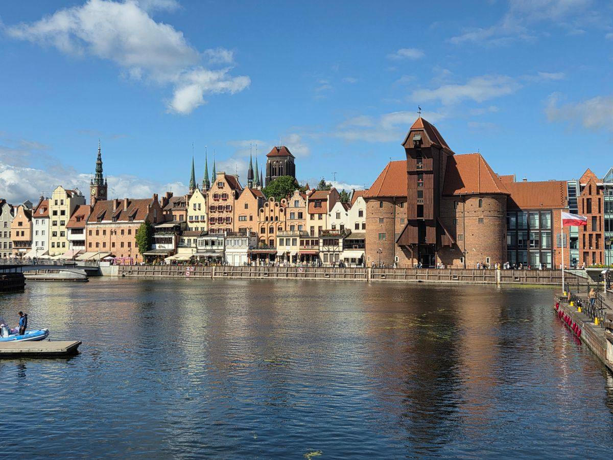 Uferpromenade an der Mottlau mit Giebelhäusern und Krantor unter blauem Himmel